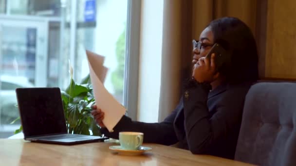 Femme d'affaires afro-américaine travaillant avec un ordinateur portable et des papiers. Fille parlant au téléphone avec un partenaire d'affaires — Video