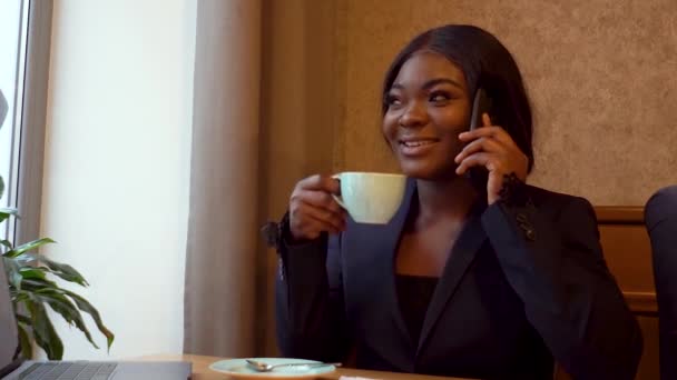 Afroamerikansk affärskvinna pratar i telefon med affärspartner och dricker kaffe — Stockvideo