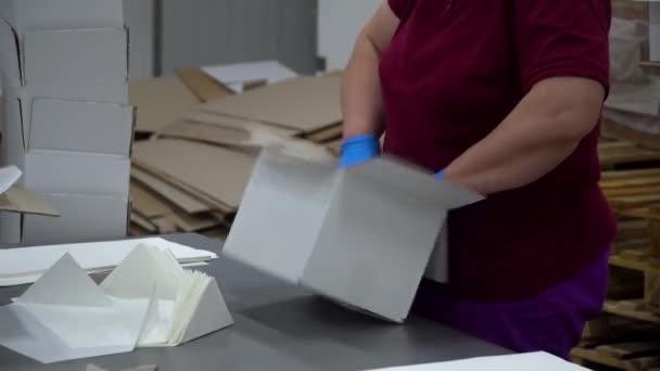 Uma operária de fábrica coloca o papel no meio de uma caixa vazia e coloca-o num transportador — Vídeo de Stock