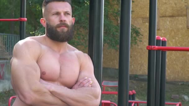 보디빌더는 근육을 보여 줍니다. 턱수염을 기르는 젊은 운동 선수 가 옥외에서 운동을 한다 — 비디오