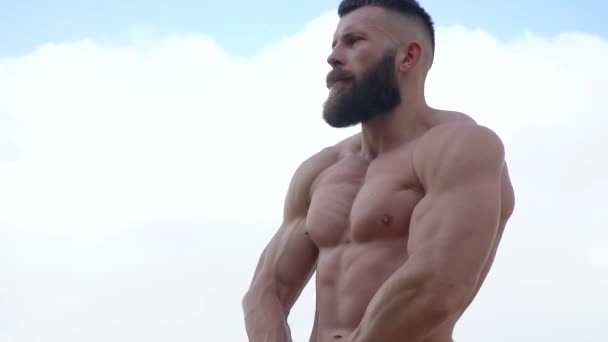 Bodybuilder visar muskler. Ung skäggig atletisk bodybuilder spelar sport utomhus — Stockvideo