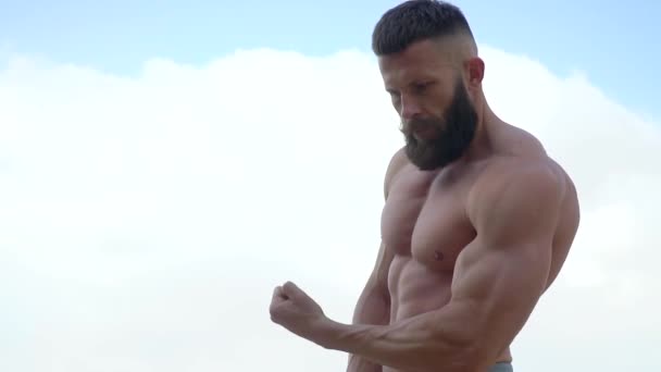 Bodybuilder visar muskler. Ung skäggig atletisk bodybuilder spelar sport utomhus — Stockvideo