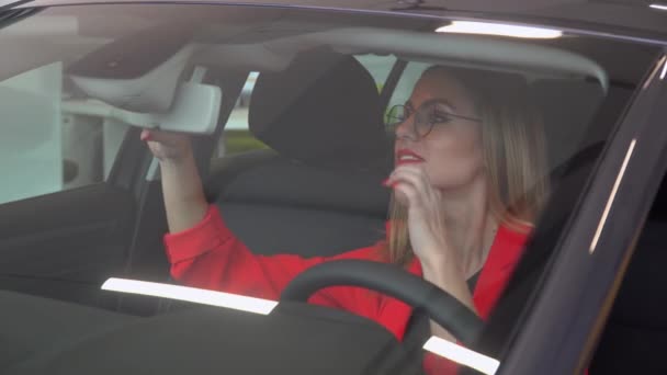 Hermosa mujer con gafas se ve en el espejo retrovisor en el coche — Vídeo de stock