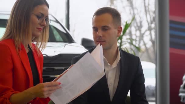 Vendeur et acheteur étudient le contrat de vente de la voiture. Belle femme achète une voiture — Video