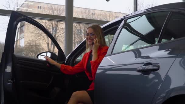 Красивая женщина разговаривает по телефону, сидя в машине в автосалоне — стоковое видео