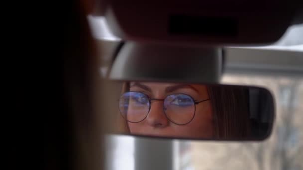 Belle femme avec des lunettes regarde dans le rétroviseur dans la voiture — Video