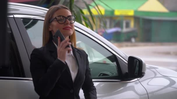 Beautiful woman with glasses talking on the phone at a car dealership — Stock Video