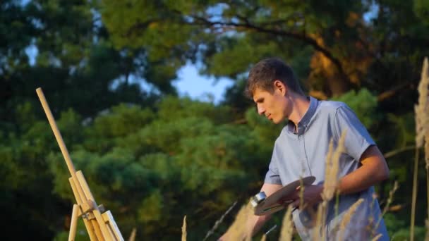 Artista masculino pinta paisaje al aire libre puesta de sol en el paisaje de la naturaleza. Un hombre pinta un cuadro — Vídeos de Stock