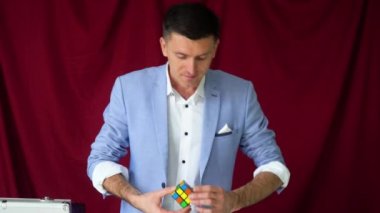 Magician in a suit shows a trick with Rubiks Cube on a vinous background