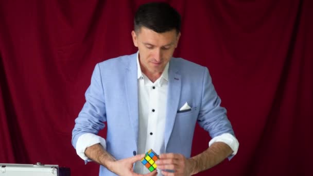Чарівник у костюмі показує трюк з Рубіксом Кубом на вінистому фоні — стокове відео