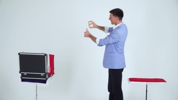 Magician in a suit shows a trick with balls on a white background — Stock Video