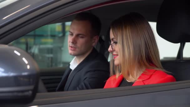 Consultor en un concesionario de automóviles presenta un coche a una mujer — Vídeos de Stock