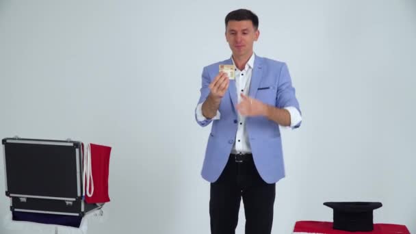 Magician in a suit shows a trick with money on a white background — Stok Video