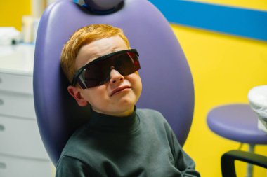 Scared red-haired boy crying at reception at dentist in dental chair. Pediatric dentistry