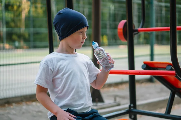 Little boy drinking water near outdoor public fitness equipment