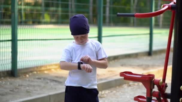 A boy on street public exercise equipment looks at his wristwatch — 비디오