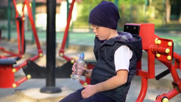 Niño pequeño bebiendo agua cerca de aparatos de fitness públicos al aire libre. Deportes para niños — Vídeos de Stock