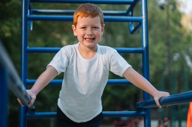 Kızıl saçlı çocuk sokakta spor egzersizleri yapıyor.