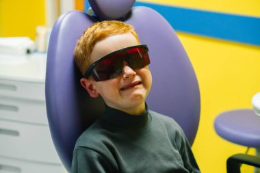 Scared red-haired boy crying at reception at dentist in dental chair. Pediatric dentistry