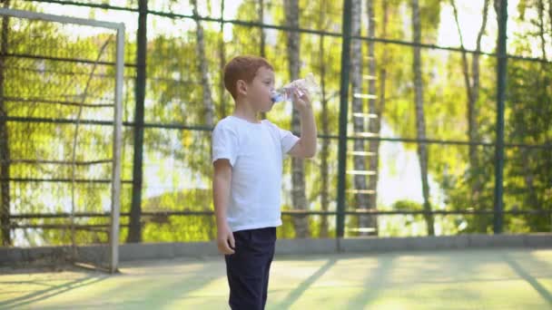 Petit garçon buvant de l'eau près de l'équipement de football public extérieur. Sports pour enfants — Video