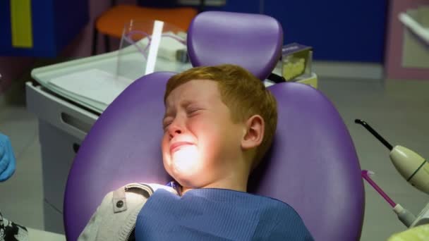 Scared red-haired boy crying at reception at dentist in dental chair. Pediatric dentistry — Stockvideo