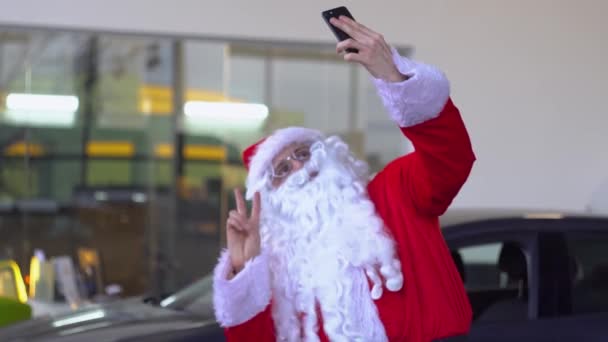 Санта Клаус робить селфі в автосалоні і показує жест "мир." — стокове відео