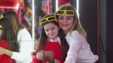 Küçük kızı olan bir kadın sinemada 3D gözlüklü bir selfie çeker.