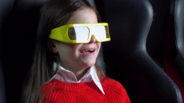 Küçük kız sinemada 3 boyutlu gözlüklü heyecanlı bir film izliyor.