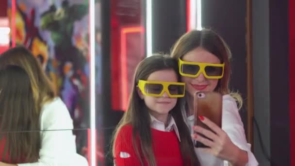 Женщина с маленькой дочерью делает селфи в кинотеатре в 3D очках — стоковое видео