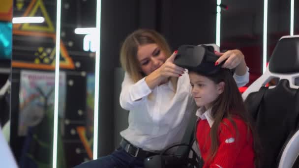 Een vrouw zet een bril op haar dochter. Vrouw en klein meisje zijn klaar om te beginnen met het spelen van virtual reality simulator — Stockvideo