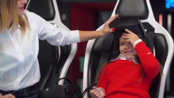 Woman and little girl are getting ready to start playing virtual reality simulator. Woman puts glasses on her daughter — 비디오