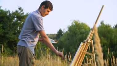 Erkek sanatçı doğa manzarasında gün batımını resmediyor. Bir adam resim çiziyor.