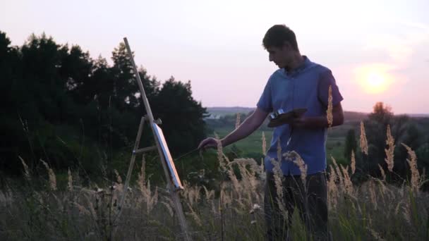 Αρσενικός καλλιτέχνης ζωγραφίζει ηλιοβασίλεμα τοπίο σε εξωτερικούς χώρους στο φυσικό τοπίο. Ένας άντρας ζωγραφίζει μια εικόνα. — Αρχείο Βίντεο