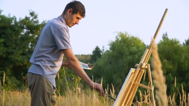 Maschio artista dipinge paesaggio tramonto all'aperto nel paesaggio della natura. Un uomo dipinge un quadro — Video Stock