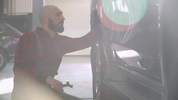 Bearded man mechanic repairing a car in car repair shop. Car service, repair and maintenance — Stock Video