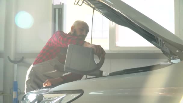 Hombre mecánico de reparación de un coche en el taller de reparación de automóviles. Mecánico vierte aceite en el motor — Vídeo de stock