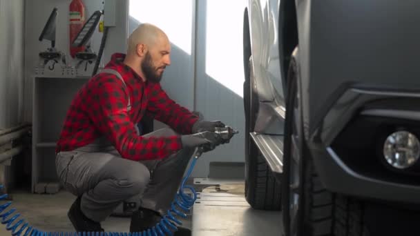 Professional mechanic in car repair shop changes wheel on passenger car — Stock Video