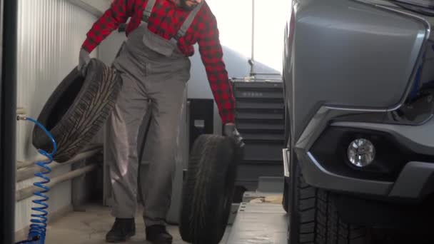 Профессиональный механик в авторемонтной мастерской меняет колесо на легковом автомобиле — стоковое видео