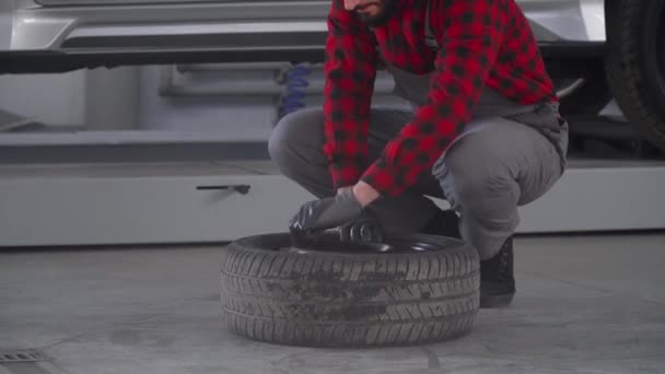 Профессиональный механик в авторемонтной мастерской меняет колесо на легковом автомобиле. Автосервис, ремонт и обслуживание — стоковое видео