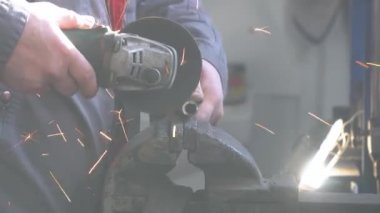 Zanaatkar atölyede disk öğütücüyle metal testeresi kesiyor. Adam çeliğin üzerinde çalıştı.