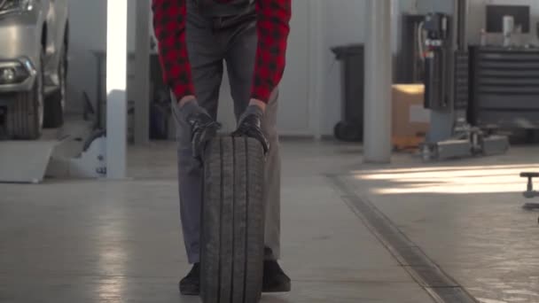 Mechanic holding a tire in garage. Professional mechanic in car repair shop changes wheel on passenger car — 비디오