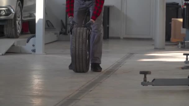 Mechanic holding a tire in garage. Professional mechanic in car repair shop changes wheel on passenger car — Stock Video