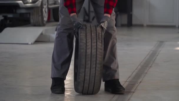 Mechanik trzymający oponę w garażu. Profesjonalny mechanik w warsztacie samochodowym zmienia koło samochodu osobowego — Wideo stockowe