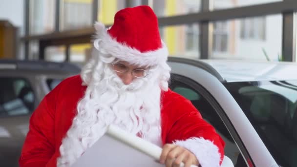 Santa Claus at a car dealership writes something down the list — Stock Video