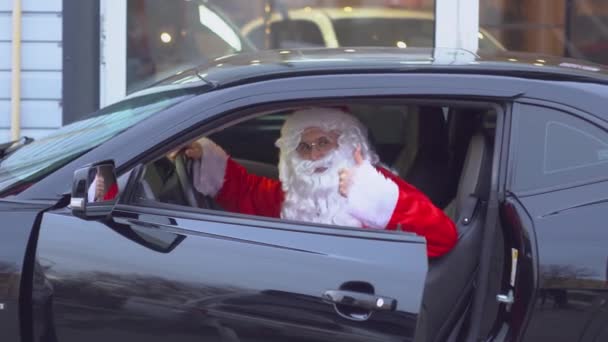 Санта-Клаус показывает жест "мир" в черном спортивном автомобиле — стоковое видео