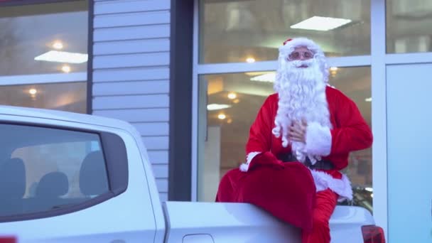 Santa Claus está sentado en la parte trasera de una camioneta. Santa en un concesionario de coches — Vídeos de Stock