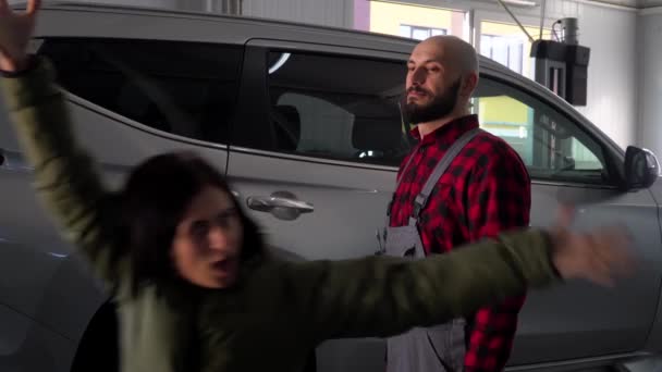 Mecánico barbudo con chica divertida en taller de reparación de coches. Servicio, reparación y mantenimiento de automóviles — Vídeos de Stock