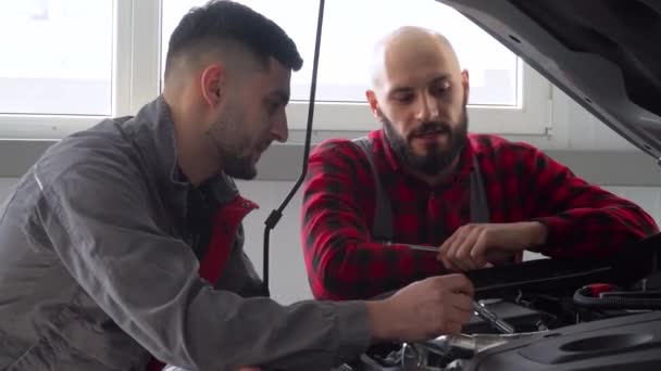 Dois mecânicos profissionais reparando um carro na oficina de reparação de automóveis. Serviço de carro, reparação e manutenção — Vídeo de Stock