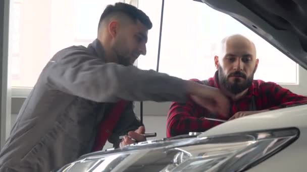 Два профессиональных механика ремонтируют автомобиль в автомастерской. Автосервис, ремонт и обслуживание — стоковое видео