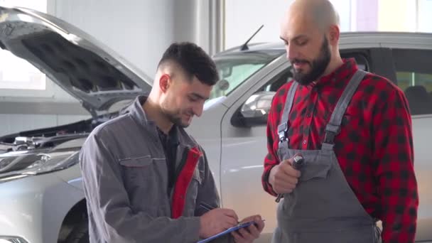 Dos mecánicos profesionales reparando un coche en el taller de reparación de automóviles. Servicio, reparación y mantenimiento de automóviles — Vídeos de Stock